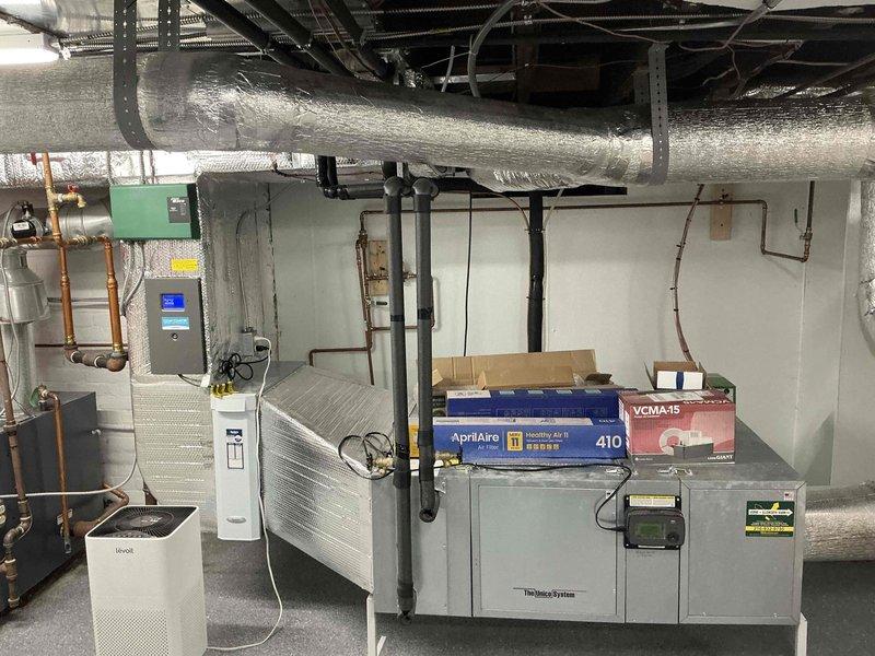 Completed HVAC equipment estimate for potential Unico system installation in basement mechanical room. Assessed existing gray HVAC unit and surrounding infrastructure including ductwork with reflective insulation, copper piping, electrical panel, and air quality equipment. Documented current system configuration and available space for proposed high-velocity air conditioning system replacement.