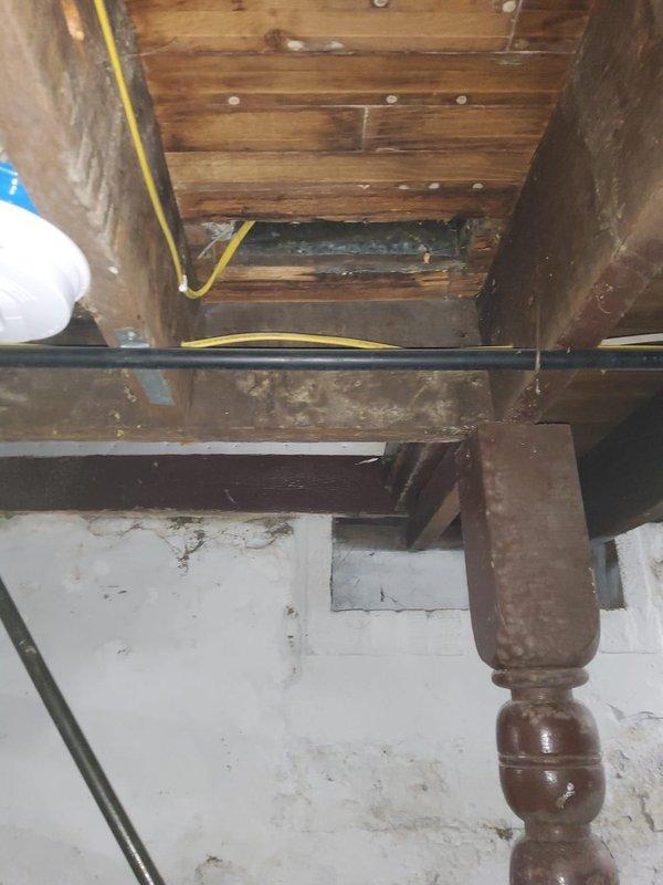 Responded to no-charge callback for assessment of insufficient airflow to back bedroom. Inspected ductwork in crawl space and attic area above affected room. Found rectangular duct opening in wooden floor framing with significant cobweb accumulation and signs of long-term neglect, indicating minimal to no air movement through this supply register. Documented exposed structural conditions, electrical wiring routing through duct space, and overall duct accessibility for future remediation work.