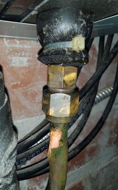 Responded to service call for mini split AC system with undetermined issue. Upon arrival, performed diagnostic inspection of outdoor unit and associated refrigerant lines. Inspected copper refrigerant piping connections showing signs of age with visible oxidation and patina buildup. Examined compression fittings connecting copper lines to flexible refrigerant hoses, noting dust accumulation on line insulation. Checked mechanical connections in basement/crawl space area where refrigerant lines enter structure. All connections found secure with no visible refrigerant leaks detected. System components inspected and documented via photography for service records.