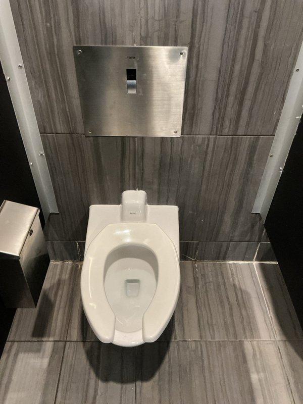 Responded to service call for toilet leaking at base during flushing in commercial restroom facility. This was the far left toilet in a three-stall configuration, with a previous service visit addressing a similar issue on another toilet in the same restroom. Upon arrival, inspected the affected floor-mounted toilet and identified water seepage at the base connection point. Removed toilet to access the wax ring seal and flange assembly. Found deteriorated wax ring allowing water to bypass the seal during flush cycles. Cleaned the toilet base and floor flange of old wax residue and debris. Inspected closet flange for cracks or damage and confirmed structural integrity. Installed new wax ring seal with proper compression. Repositioned toilet onto flange, ensuring proper alignment with mounting bolts. Torqued closet bolts to manufacturer specifications to create watertight seal without over-compression. Reconnected water supply line and tested flush mechanism multiple times to verify leak