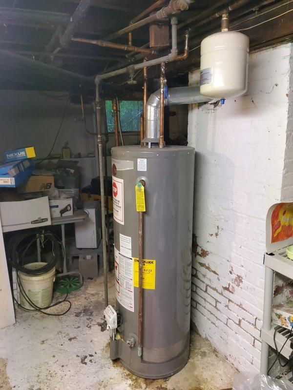 Completed standard water heater flush and fill service on natural gas tanked unit located in basement utility room. Upon arrival, identified active leak from bottom of tank, indicating internal corrosion and tank failure. Documented existing conditions with photographs showing water heater installation, surrounding plumbing connections, expansion tank, and copper supply lines. Due to leak from tank bottom, advised customer that unit requires replacement as this condition is not repairable and poses risk of catastrophic failure.