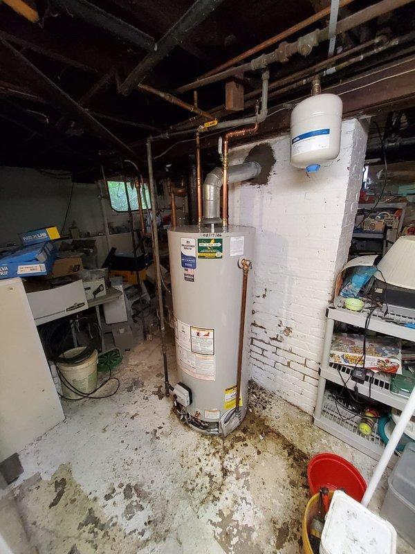 Completed standard water heater flush and fill service on natural gas tanked unit located in basement utility room. Upon arrival, identified active leak from bottom of tank, indicating internal corrosion and tank failure. Documented existing conditions with photographs showing water heater installation, surrounding plumbing connections, expansion tank, and copper supply lines. Due to leak from tank bottom, advised customer that unit requires replacement as this condition is not repairable and poses risk of catastrophic failure.