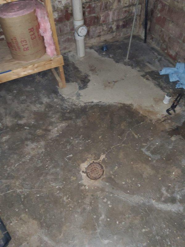 Responded to recurring main drain line backup causing basement flooding. Upon arrival, standing water had receded. Customer reported repeated backups with suspected root intrusion in main sewer line. Assessed basement area showing evidence of previous water damage on concrete floor with visible staining and moisture patterns. Located main drain cleanout access point with white PVC pipe and cleanout fitting on basement wall. Documented existing conditions including floor drain and plumbing configuration. Based on recurring nature of backups and customer history of blockages, recommended scheduling follow-up service with specialized equipment and additional technician for comprehensive main line cleaning and video camera inspection to confirm root intrusion and determine extent of blockage in sewer line.