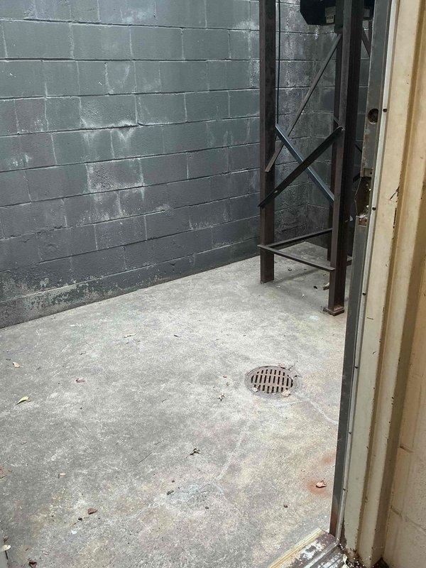 Conducted on-site assessment for mini split installation in small basement server room. Evaluated existing space conditions including concrete block wall construction, floor drain location, and potential routing for refrigerant lines and condensate drainage. Documented exterior wall access point and overhead structure for outdoor condenser unit placement, noting corrugated metal roof overhang and existing ductwork configuration that may impact installation requirements.