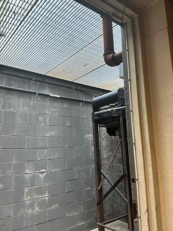 Conducted on-site assessment for mini split installation in small basement server room. Evaluated existing space conditions including concrete block wall construction, floor drain location, and potential routing for refrigerant lines and condensate drainage. Documented exterior wall access point and overhead structure for outdoor condenser unit placement, noting corrugated metal roof overhang and existing ductwork configuration that may impact installation requirements.