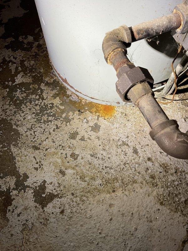 Responded to service call for leaking water heater in 112-year-old residence. Upon inspection, identified significant water leakage at base connections with visible corrosion on threaded pipe fittings and elbow joints, evidenced by orange-rust staining on concrete floor beneath unit. Assessed aged metal plumbing infrastructure showing oxidation and deterioration consistent with extended service life. Performed necessary repairs to eliminate active leak, addressed corroded connections, and verified proper operation of unit. System tested and confirmed leak-free upon completion.