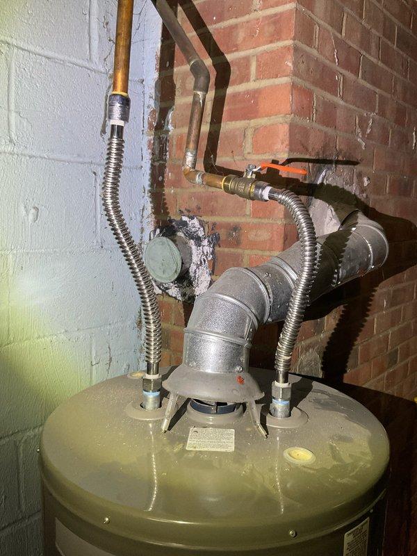 Responded to service call for leaking water heater in 76-year-old residential property. Upon inspection, identified active leak from deteriorated tank connections and visible corrosion on metal fittings at top of unit. Assessed flexible metallic supply lines, copper piping connections, and shutoff valves for integrity and proper function. Documented existing installation showing corrugated stainless steel flex connectors, orange-handled isolation valve, and galvanized vent pipe assembly. Given age of home and condition of water heater with compromised tank integrity and corroded fittings, recommended full unit replacement to prevent further water damage and ensure safe operation.