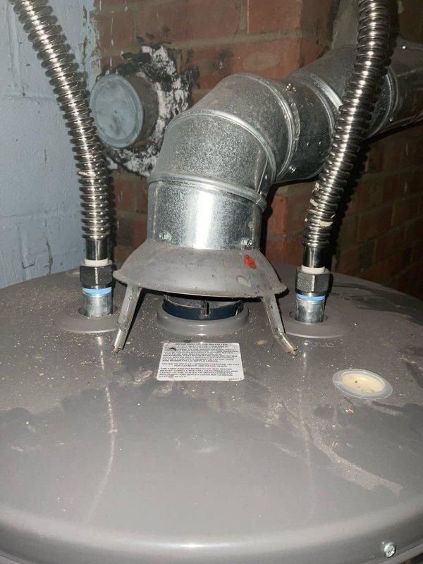 Responded to service call for leaking water heater in 76-year-old residential property. Upon inspection, identified active leak from deteriorated tank connections and visible corrosion on metal fittings at top of unit. Assessed flexible metallic supply lines, copper piping connections, and shutoff valves for integrity and proper function. Documented existing installation showing corrugated stainless steel flex connectors, orange-handled isolation valve, and galvanized vent pipe assembly. Given age of home and condition of water heater with compromised tank integrity and corroded fittings, recommended full unit replacement to prevent further water damage and ensure safe operation.