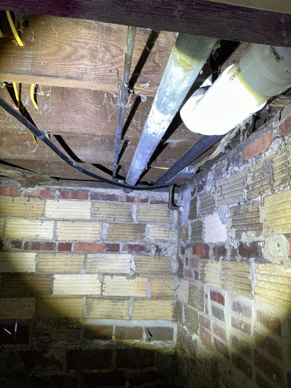 Responded to report of rust spots and leaking on basement sewage stack. Upon inspection, identified corrosion and active leak on cast iron waste stack near floor penetration. Documented existing conditions showing deteriorated pipe sections with visible rust staining on masonry wall and floor area. Photographed affected plumbing infrastructure including waste stack, adjacent water lines, and structural mounting points for assessment and repair recommendation purposes.