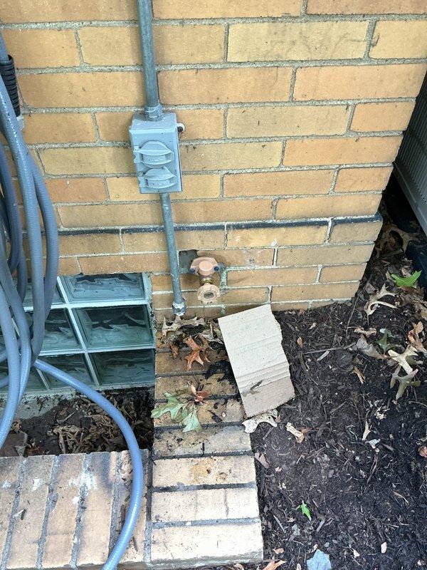 Responded to service call for exterior hose bib leaking into basement when in use. Performed complimentary plumbing assessment of rear outdoor spigot installation. Upon inspection, identified brass spigot mounted on yellow brick exterior foundation wall with evidence of water infiltration issues. Examined interior basement area and located corresponding plumbing connections behind spigot location. Found deteriorated pipe penetration through foundation wall with visible water staining and corrosion on interior mechanical components. Spider webs and undisturbed conditions indicated chronic seepage issue rather than recent failure. Documented exterior spigot installation and interior basement conditions with photographs showing compromised seal at wall penetration point. Advised homeowner of findings and provided recommendations for proper repair to prevent continued water intrusion into basement space.