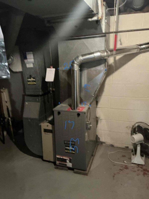 Completed on-site evaluation for HVAC system replacement in residential basement mechanical room. Assessed existing furnace unit and ductwork configuration, documented current equipment specifications and installation layout. Photographed existing system components including furnace, metal supply ductwork with multiple elbows, and surrounding utility equipment to prepare comprehensive replacement estimate.