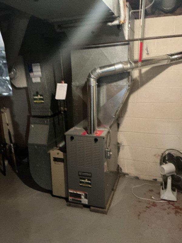 Completed on-site evaluation for HVAC system replacement in residential basement mechanical room. Assessed existing furnace unit and ductwork configuration, documented current equipment specifications and installation layout. Photographed existing system components including furnace, metal supply ductwork with multiple elbows, and surrounding utility equipment to prepare comprehensive replacement estimate.