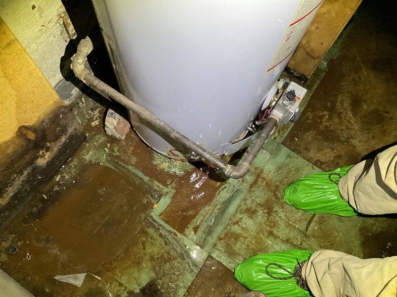 Responded to emergency service call for severely leaking tanked water heater causing extensive water damage and hazardous mold conditions in basement utility area. Upon arrival, found standing water pooling around base of water heater with significant floor saturation and visible deterioration of concrete surfaces. Shut off water supply to failed water heater to stop active leak and prevent further water intrusion. Documented hazardous conditions including contaminated standing water, moisture damage to surrounding surfaces, and compromised indoor air quality requiring protective respiratory equipment during service.