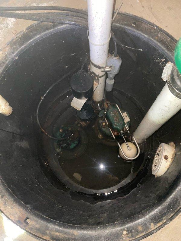 Responded to service call for AquaNot Active 500 battery backup sump pump system experiencing daily test mode failures with recurring alarm activation. System had been malfunctioning for several weeks, requiring customer to manually silence alarms. Inspected sump pump basin containing green primary pump unit with float switch assembly and associated PVC discharge piping. Evaluated AquaNot control panel mounted on wall, examining system ready indicators, battery status, DC pump operation, AC power supply, and high water switch functionality. Tested operational and silence buttons on control unit. Assessed battery backup component and electrical connections. Documented existing installation configuration including pump placement, plumbing connections, and control system setup through photographic evidence for service records.
