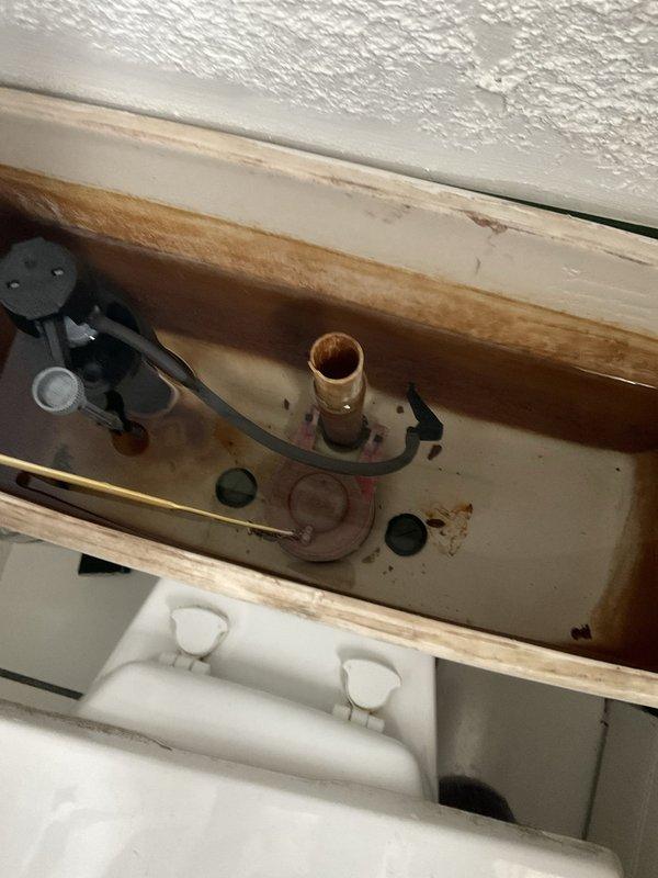 Responded to water leak investigation in 1920s-era residential property. Upon inspection, identified toilet tank as source of leak with significant water damage to surrounding wooden framing and structural components. Tank interior showed extensive brown water staining, mineral deposits, and discolored water indicating chronic leak and corrosion of flush valve assembly. Documented deteriorated wooden framing compromised by long-term moisture exposure, rust staining on metal components, and sediment buildup in tank bottom. Recommended replacement of corroded flush valve system and repair of water-damaged structural framing to prevent further deterioration.