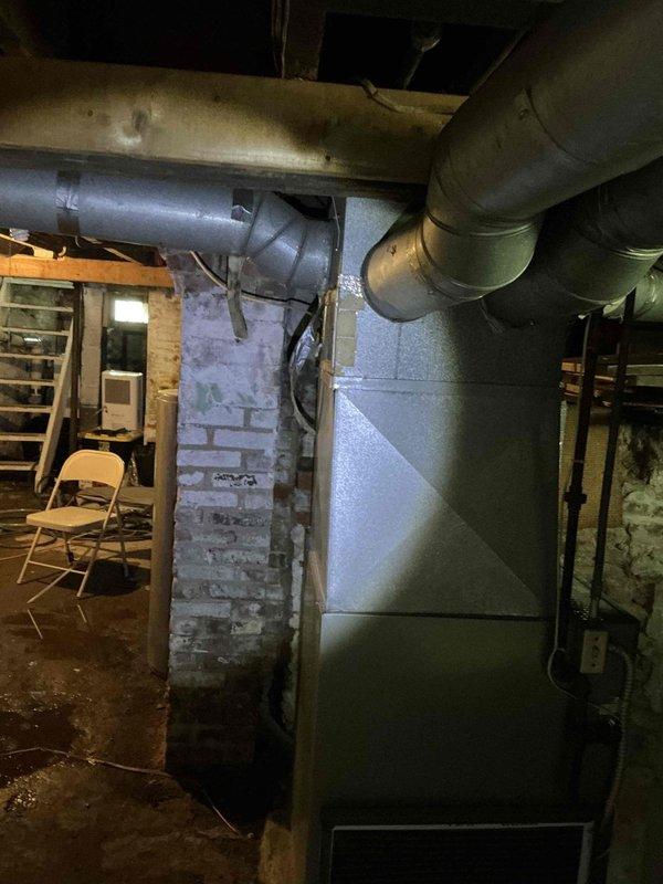 Conducted comprehensive HVAC system evaluation in basement utility area to provide replacement estimate for existing furnace and options for adding cooling capacity. Assessed current gray metal furnace unit positioned against foundation walls with overhead ductwork distribution system. Evaluated space constraints, existing duct infrastructure, electrical service capacity, and gas line configuration to determine optimal cooling solution. Presented homeowner with multiple options including traditional split system air conditioning installation versus ductless mini-split system based on existing conditions and customer needs.