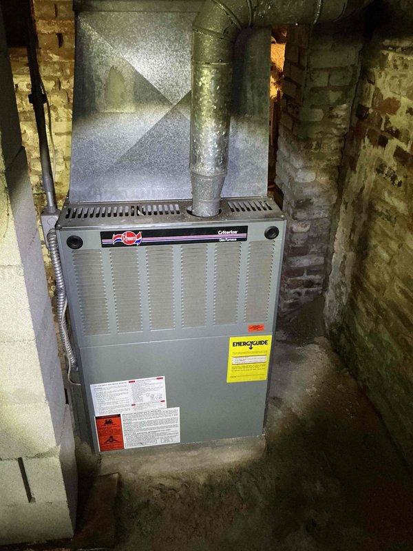 Conducted comprehensive HVAC system evaluation in basement utility area to provide replacement estimate for existing furnace and options for adding cooling capacity. Assessed current gray metal furnace unit positioned against foundation walls with overhead ductwork distribution system. Evaluated space constraints, existing duct infrastructure, electrical service capacity, and gas line configuration to determine optimal cooling solution. Presented homeowner with multiple options including traditional split system air conditioning installation versus ductless mini-split system based on existing conditions and customer needs.