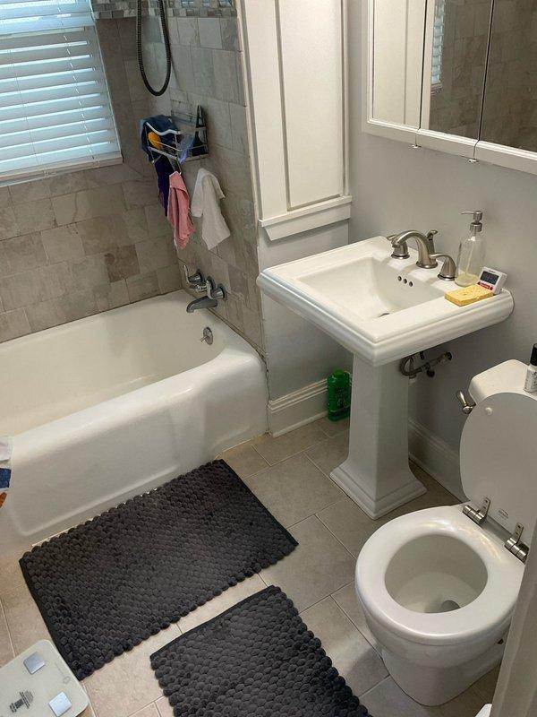 Responded to water leak originating from second-floor bathroom and penetrating into foyer below in century-old residential property. Upon arrival, conducted thorough inspection of bathroom fixtures including pedestal sink, bathtub with shower assembly, and toilet to identify source of leak. Examined all visible plumbing connections, drain assemblies, and supply lines. Inspected underside of pedestal sink where drainage pipes penetrate floor, noting aged plumbing components and floor penetration points. Assessed condition of drain collar, pipe connections, and surrounding subfloor area for signs of active water intrusion. Documented existing conditions through photographic evidence showing bathroom layout, fixture placement, and critical plumbing connection points beneath sink where pipes pass through flooring into space below. Leak source identified and necessary repairs completed to prevent continued water damage to lower level.