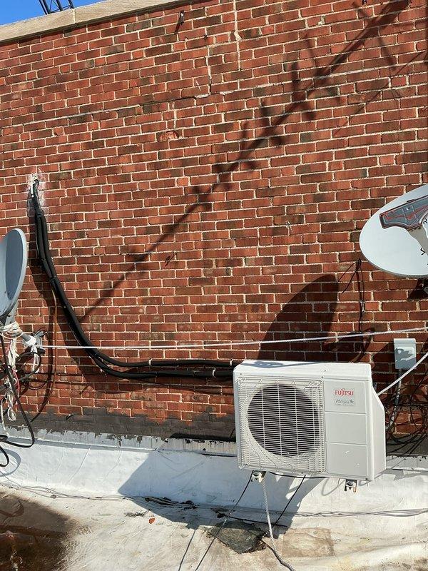 Completed HVAC estimate for replacement of existing air conditioning system in mechanical room. Evaluated Fujitsu split-type air conditioner condenser unit mounted on exterior brick wall with white concrete base. Unit operates on 200/230V electrical specifications and is connected via black electrical conduit running along building exterior. Documented equipment specifications, installation location, mounting configuration on metal brackets, and overall system condition. Photographed condenser unit, manufacturer specification label, electrical connections, and surrounding installation area to provide comprehensive assessment for replacement recommendation.