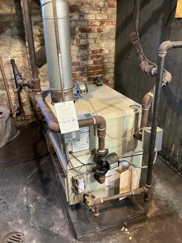Conducted comprehensive assessment of aging 30-year-old commercial-grade boiler system located in basement mechanical room with exposed brick construction. Upon inspection, identified unit manufactured by Adiator Corporation showing significant age-related deterioration and requiring extensive repairs that would be cost-prohibitive relative to equipment value. Documented all specification label information including maximum water pressure ratings, relief valve capacity, input BTU/HR, natural gas specifications, and serial number data. Photographed complete system configuration including copper piping connections, circulation pump assembly with electrical wiring, vertical venting arrangement, and overall installation layout to support replacement recommendation. Prepared detailed estimate for commercial-sized boiler replacement given the advanced age of existing equipment and anticipated ongoing maintenance costs.