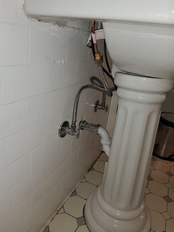 Repaired dripping bathroom faucet and replaced deteriorated supply line inside wall cavity behind pedestal sink. Accessed water supply lines through existing wall opening, installed new braided stainless steel supply line with proper fittings, and verified all connections were leak-free and operating correctly.