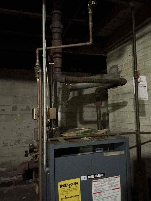 Completed comprehensive boiler inspection in mechanical room. System evaluated included blue residential boiler unit with associated piping network showing age-related wear and oxidation on multiple pipe runs. Documented current equipment condition, piping configuration, and overall system status through photographic records for maintenance planning purposes.