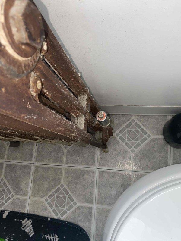 Responded to service call for leaking radiator in older residential property. Upon inspection, found severely corroded radiator valve and supply piping with extensive rust and oxidation throughout metal components. The corrosion had compromised pipe integrity at connection points, resulting in active leak. Documented existing conditions with photographs showing deteriorated plumbing fixtures, corroded pipe fittings with hexagonal couplings, and significant mineral buildup on all metal surfaces. Recommended replacement of affected piping section and valve assembly due to advanced corrosion beyond serviceable condition.