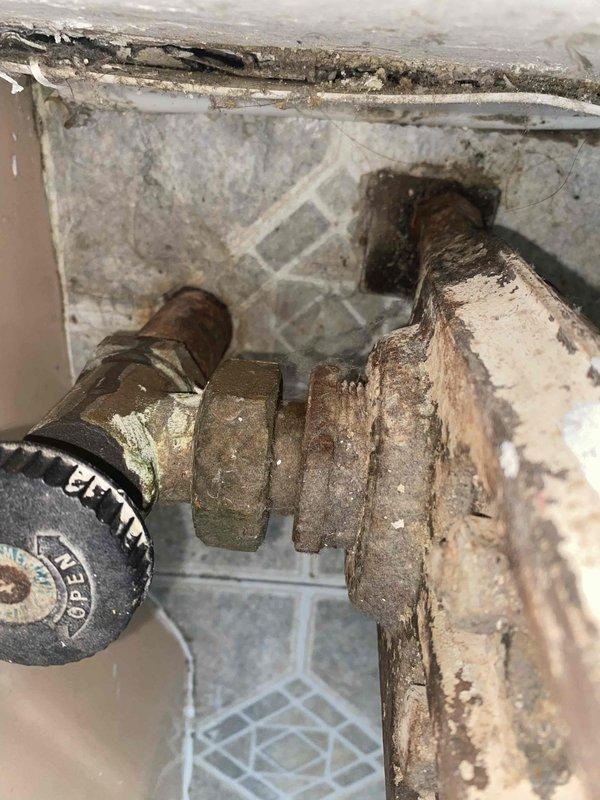 Responded to service call for leaking radiator in older residential property. Upon inspection, found severely corroded radiator valve and supply piping with extensive rust and oxidation throughout metal components. The corrosion had compromised pipe integrity at connection points, resulting in active leak. Documented existing conditions with photographs showing deteriorated plumbing fixtures, corroded pipe fittings with hexagonal couplings, and significant mineral buildup on all metal surfaces. Recommended replacement of affected piping section and valve assembly due to advanced corrosion beyond serviceable condition.