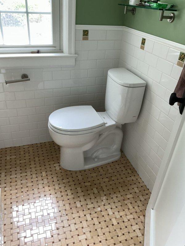 Completed installation of two toilets in separate bathroom locations. First bathroom featured white ceramic toilet installed in corner setting with existing subway tile wainscoting and basket-weave mosaic floor. Second bathroom installation included toilet positioning adjacent to new vanity setup. Set and secured vanity unit with light wood finish featuring vertical slat detailing, integrated white rectangular sink, and matte black single-handle faucet. Ensured proper connections, verified water supply lines, tested flush mechanisms and faucet operation for leaks, and confirmed all fixtures level and properly sealed.