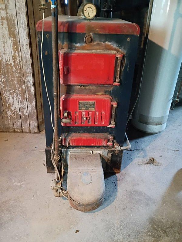 Responded to service call for a century-old United States Radiator Company boiler (Model: Redtop) requiring conversion repair. Upon inspection, found extensive deterioration throughout the unit including significant rust on red-painted access panels, corroded piping, and deteriorated electrical wiring. Documented the condition of the aging equipment with photographs showing the three-panel front access configuration, pressure gauge assembly, and overall structural degradation of the heating system.