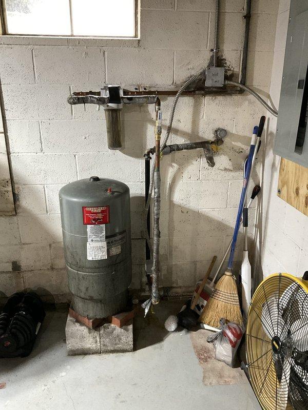 Conducted free estimate for water softener installation in basement utility area. Assessed existing plumbing configuration including current pressure tank, filtration system, and piping layout to determine optimal placement and integration requirements for new water softening equipment. Documented existing conditions showing signs of hard water damage, corrosion on pressure vessel, and floor moisture staining, confirming need for water treatment solution.