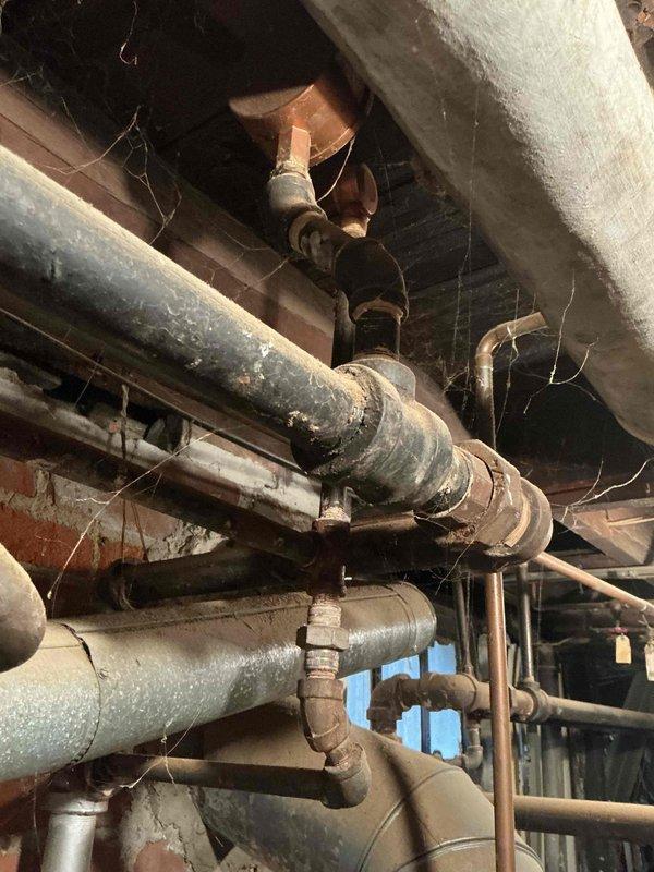 Completed comprehensive boiler replacement estimate for residential property. Assessed existing heating system infrastructure, including aged piping network with mixed materials showing significant wear, deteriorated insulation, and cobweb accumulation indicating limited recent maintenance. Documented current mechanical room configuration featuring vertical ductwork, water heater placement, and copper and galvanized piping with multiple joints and connections. Photographed existing conditions to support equipment sizing recommendations and scope of work development for complete boiler system replacement.
