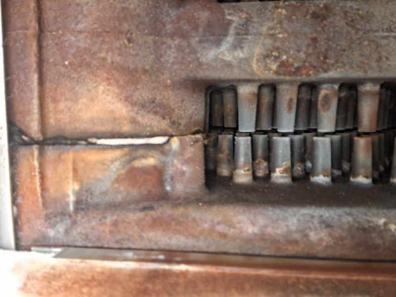 Performed routine maintenance inspection on a 7-year-old hot water boiler system. Documented extensive corrosion and rust present on burner assembly components and associated piping, with visible oxidation on metal tubes and deterioration of heating elements against refractory brick surfaces. Confirmed operational status of unit at time of service visit.
