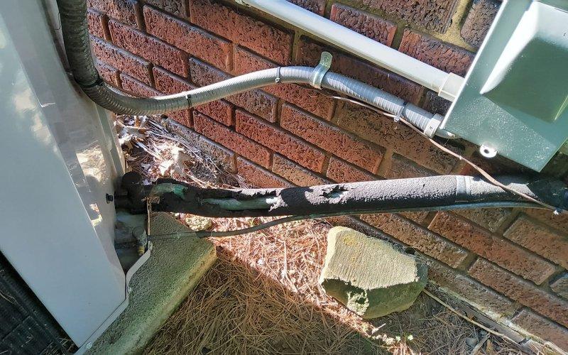 Performed inspection of outdoor HVAC system and identified significant deterioration of refrigerant line insulation on the vapor line running from the house to the condenser unit. The insulation wrapping showed extensive damage with missing pieces and torn sections exposing the underlying copper piping. Documented the condition with photographs showing the compromised insulation on both horizontal and diagonal refrigerant line runs. Advised that the damaged insulation requires complete replacement to prevent energy loss, maintain system efficiency, and protect against condensation issues that could lead to water damage or reduced cooling performance.