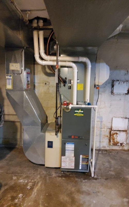 Responded to no cooling call on 20-year-old residential air conditioning system. Upon arrival, performed diagnostic assessment of outdoor condenser unit and indoor air handler/furnace assembly. Inspected 20-year-old outdoor unit positioned on concrete paver patio against perimeter fence, checking for power supply, refrigerant levels, compressor operation, and condenser fan functionality. Evaluated indoor equipment in basement utility room, including furnace, ductwork connections, and associated HVAC components. Noted age-related wear on system components and assessed overall system condition. Documented equipment configuration with outdoor condenser unit and basement-mounted air handler setup connected via refrigerant lines and electrical systems. System evaluated for repair viability versus replacement recommendation given advanced age exceeding typical 15-year service life expectancy for residential AC equipment.