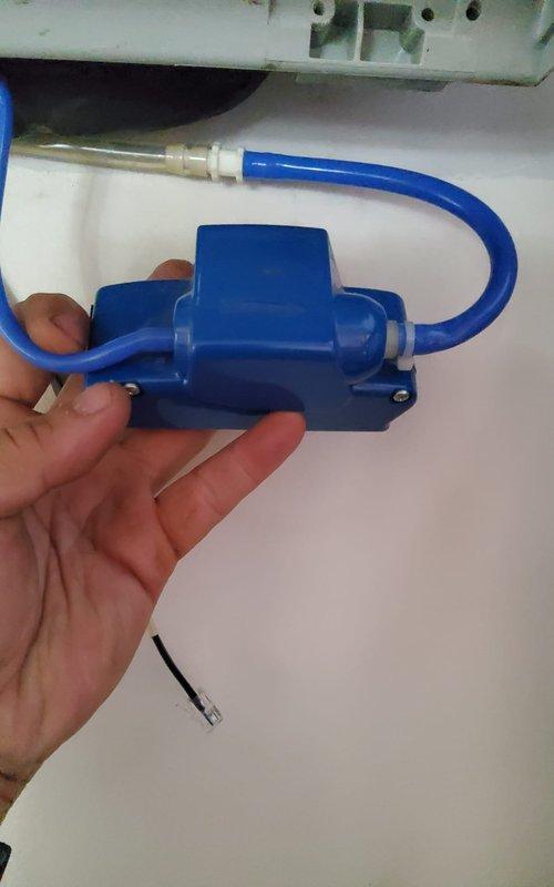 Responded to service call for noisy mini-split air conditioning unit. Upon inspection, identified malfunctioning condensate pump as source of operational noise. Removed defective blue condensate pump assembly with dual drainage tubes and brass fittings, replaced with new unit, and verified proper drainage function. Tested indoor wall-mounted evaporator unit for normal operation, confirmed quiet performance and proper temperature display functionality.