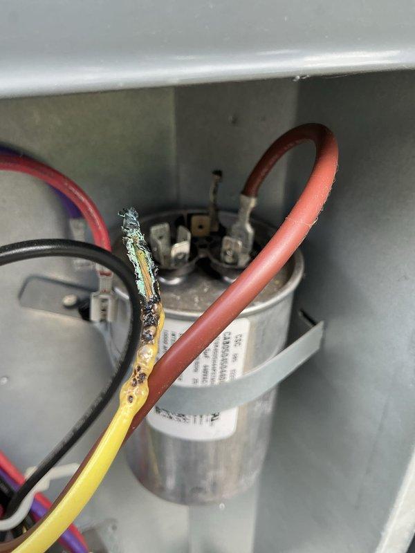 Responded to service call for non-operational 2-year-old central air conditioning system. Upon inspection, discovered severe thermal damage to capacitor wiring, with yellow wire insulation melted and charred, exposing bare conductor. Replaced failed dual-run capacitor and damaged wire connections. System tested successfully and restored to full operation.