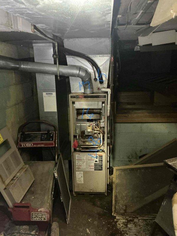 Conducted furnace replacement estimate in basement mechanical room. Inspected existing vertically-oriented furnace unit with open access panel, evaluating internal components including burners, blower assembly, wiring, valves, and mechanical connections. Assessed condition of gray metal ductwork extending from unit and connecting supply/return air distribution system. Documented equipment specifications from manufacturer labels and data plates. Photographed installation location, existing ductwork configuration, electrical connections, and overall mechanical room layout to prepare comprehensive replacement proposal.