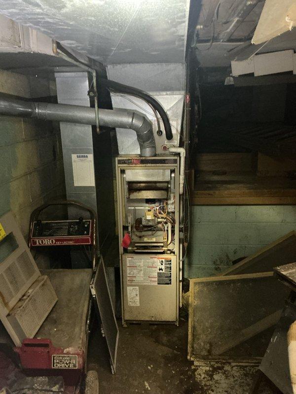 Conducted furnace replacement estimate in basement mechanical room. Inspected existing vertically-oriented furnace unit with open access panel, evaluating internal components including burners, blower assembly, wiring, valves, and mechanical connections. Assessed condition of gray metal ductwork extending from unit and connecting supply/return air distribution system. Documented equipment specifications from manufacturer labels and data plates. Photographed installation location, existing ductwork configuration, electrical connections, and overall mechanical room layout to prepare comprehensive replacement proposal.