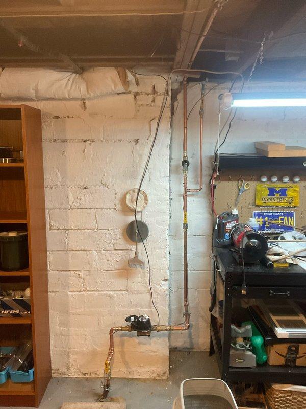 Removed existing galvanized water supply line from meter to copper transition point and replaced with PEX piping system. Installed 30 feet of 1/2" blue PEX with brass adapters and fittings, including a 1/2" brass 90-degree elbow on the riser under stairs. Abandoned existing cold water galvanized line from utility tub and rerouted supply from main trunk line to front exterior spigot. Installed new frost-free hose bib at exterior location. Completed installation included three 1/2" PEX 90-degree fittings, two male adapters, one 1/2" brass 90-degree elbow, one 1/2" brass plug, and three 1/2" press valves for shutoff capability throughout the system.