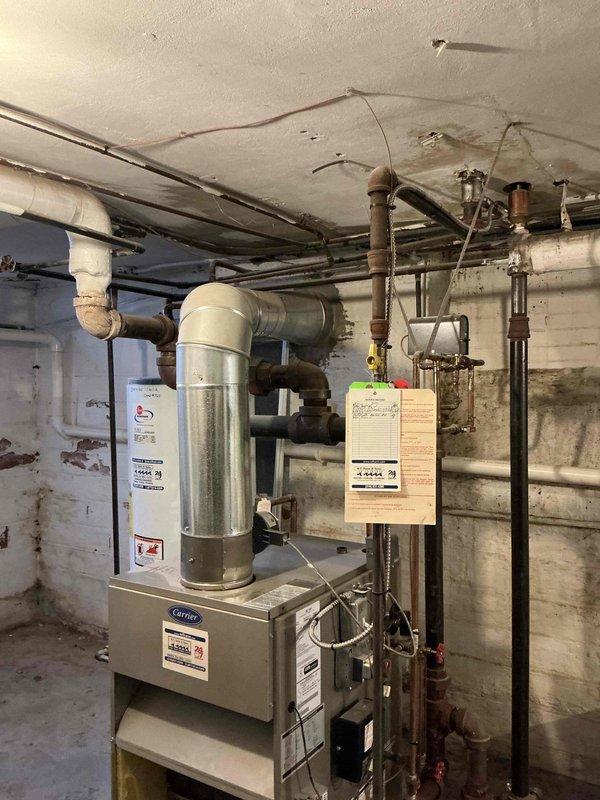 Conducted on-site assessment of existing Carrier heating system in basement mechanical room to provide steam boiler replacement estimate. Evaluated current equipment configuration, including furnace unit, ductwork, expansion tank, and associated plumbing connections. Documented existing installation with photographs showing multiple aged pipes with visible rust and corrosion on metal fittings, water-stained ceiling areas, and overall mechanical room layout. Assessed compatibility requirements for new steam boiler installation, including necessary pipe connections, venting requirements, and spatial considerations for equipment replacement in the existing footprint.