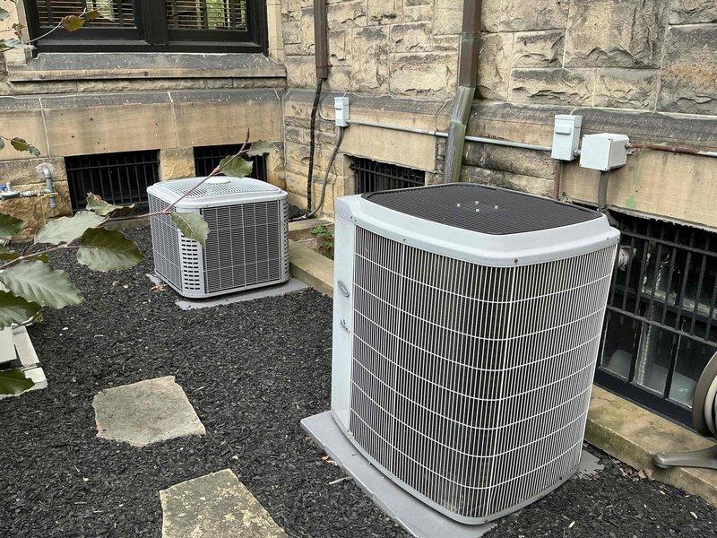 Completed comprehensive HVAC system replacement estimate for Unico system installation. Evaluated existing dual outdoor condensing units positioned on gravel pad against stone foundation and assessed interior air handler with furnace setup currently installed in carpeted living space. Documented equipment specifications, electrical disconnects, drainage configuration with PVC piping, and ductwork connections including flexible ducting and silver foil-wrapped components to provide accurate replacement pricing and installation requirements.