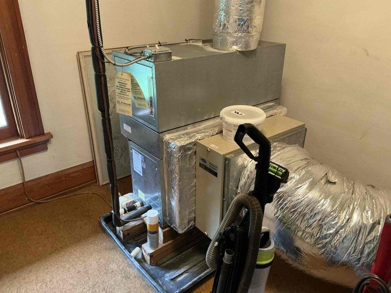 Completed comprehensive HVAC system replacement estimate for Unico system installation. Evaluated existing dual outdoor condensing units positioned on gravel pad against stone foundation and assessed interior air handler with furnace setup currently installed in carpeted living space. Documented equipment specifications, electrical disconnects, drainage configuration with PVC piping, and ductwork connections including flexible ducting and silver foil-wrapped components to provide accurate replacement pricing and installation requirements.