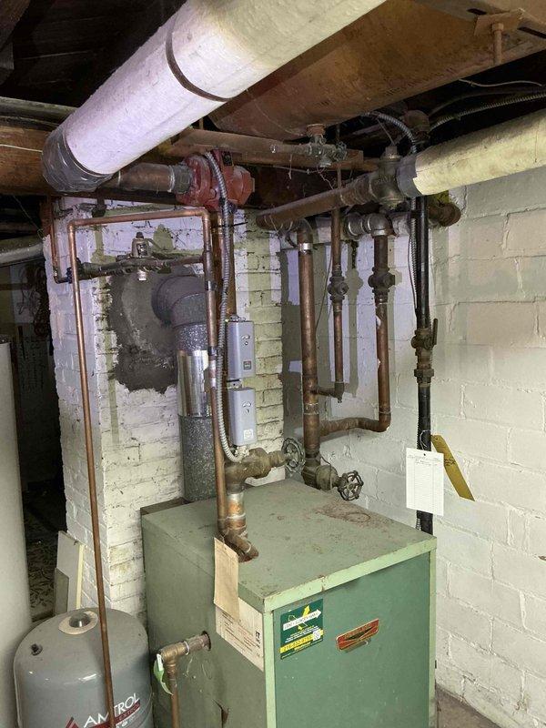 Conducted estimate for replacement of aging residential boiler system in basement mechanical room. Assessed existing light green boiler unit with associated copper piping network, expansion tank, circulator pump, and zone valves showing significant wear and oxidation consistent with extended service life. Documented current system configuration including connection points, venting arrangement with PVC flue pipe, pressure tank placement, and integration with existing hydronic heating distribution system. Photographed equipment condition, piping layout, and installation environment to prepare comprehensive replacement proposal. Provided homeowner with equipment options and scheduling recommendations for system replacement.