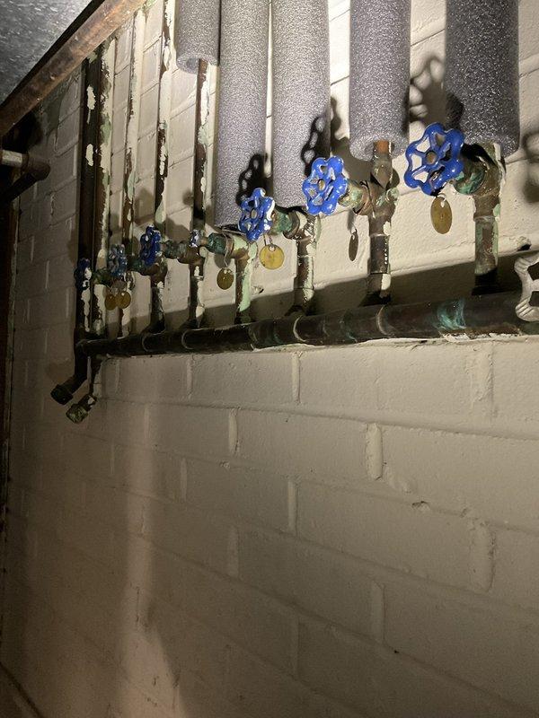 Performed comprehensive plumbing inspection for new homeowner, with primary focus on water heater system and associated plumbing infrastructure. Inspected main water supply lines, shut-off valves, water meter, and distribution piping throughout mechanical space. Evaluated condition of existing gate valves with identification tags, copper supply lines with foam insulation, and brass fittings showing age-related patina and oxidation. Documented current state of plumbing system including water heater connections, supply and return lines, and shut-off valve functionality for homeowner's records and future maintenance planning.
