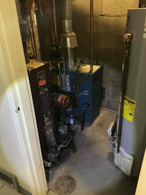 Responded to service call for non-operational oil-fired boiler system in residential basement. Conducted comprehensive assessment of existing blue boiler unit with red burner assembly, associated controls, flue system, and connected piping. Documented current equipment condition and configuration including control panel, circulator components, copper piping connections, and exhaust venting to provide estimate for necessary repairs or replacement.