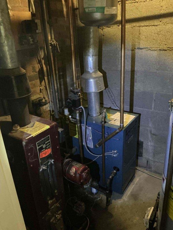 Responded to service call for non-operational oil-fired boiler system in residential basement. Conducted comprehensive assessment of existing blue boiler unit with red burner assembly, associated controls, flue system, and connected piping. Documented current equipment condition and configuration including control panel, circulator components, copper piping connections, and exhaust venting to provide estimate for necessary repairs or replacement.