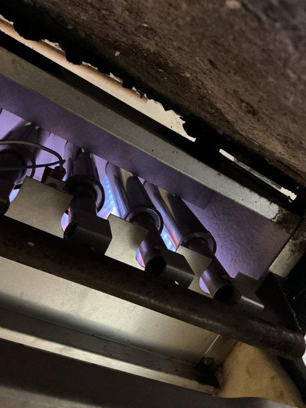 Performed annual maintenance on 7-year-old boiler system operating without reported issues. Inspected gas burner assembly with active combustion showing proper blue flame pattern across all burner tubes. Observed significant soot and debris accumulation on heat exchanger surfaces above burner assembly, indicating normal aging but requiring monitoring. Examined aged copper piping system displaying heavy oxidation and green patina throughout vertical and horizontal runs. Verified all mechanical connections, gauges, and system components for proper operation. Documented equipment condition through photography for maintenance records. System operating within normal parameters upon completion of tune-up procedures.