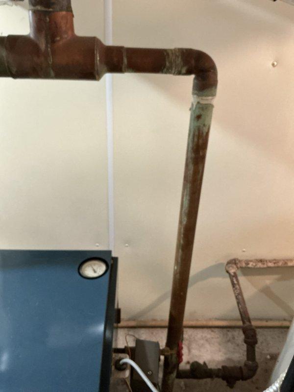 Performed annual maintenance on 7-year-old boiler system operating without reported issues. Inspected gas burner assembly with active combustion showing proper blue flame pattern across all burner tubes. Observed significant soot and debris accumulation on heat exchanger surfaces above burner assembly, indicating normal aging but requiring monitoring. Examined aged copper piping system displaying heavy oxidation and green patina throughout vertical and horizontal runs. Verified all mechanical connections, gauges, and system components for proper operation. Documented equipment condition through photography for maintenance records. System operating within normal parameters upon completion of tune-up procedures.