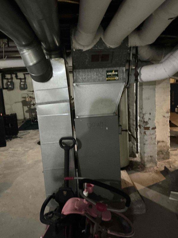 Conducted furnace replacement estimate for residential forced-air heating system located in basement mechanical room. Assessed existing gray metal furnace unit with connected ductwork, PVC condensate drainage lines, and galvanized plenum, documenting current equipment configuration and installation requirements for replacement unit.